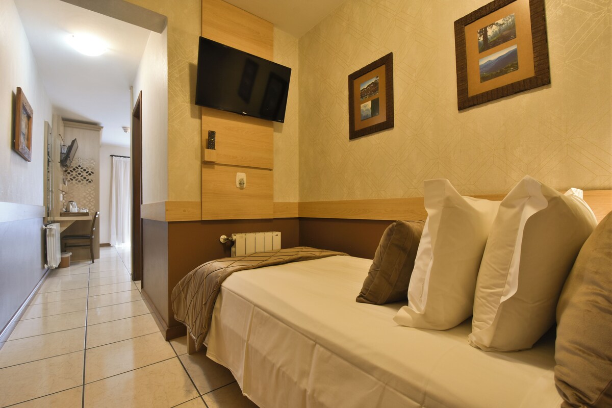 A hotel room with a bed, a TV mounted on the wall, and a bathroom visible in the background.