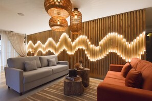 A modern living room with a grey sofa, an orange armchair, and a wooden wall with a light wave pattern. - Pousada Belluno (Gramado)