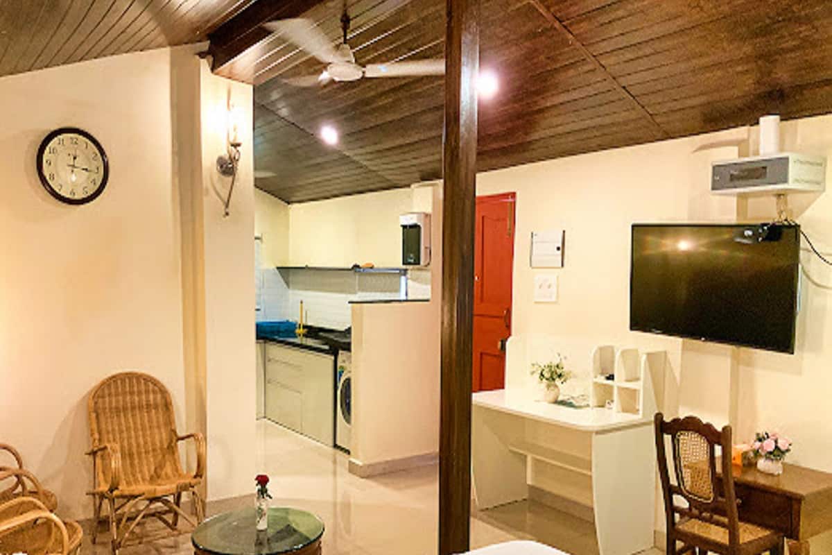 Habitació d'hotel amb llit, escriptori i cadira, televisió, rellotge i una cuineta al fons.