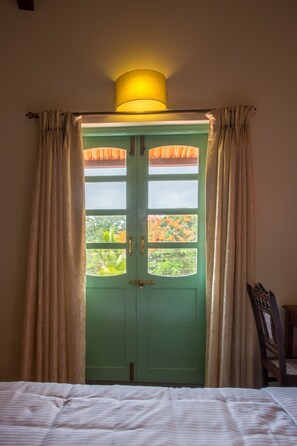 A room with a green door, beige curtains, and a bed with white bedding.