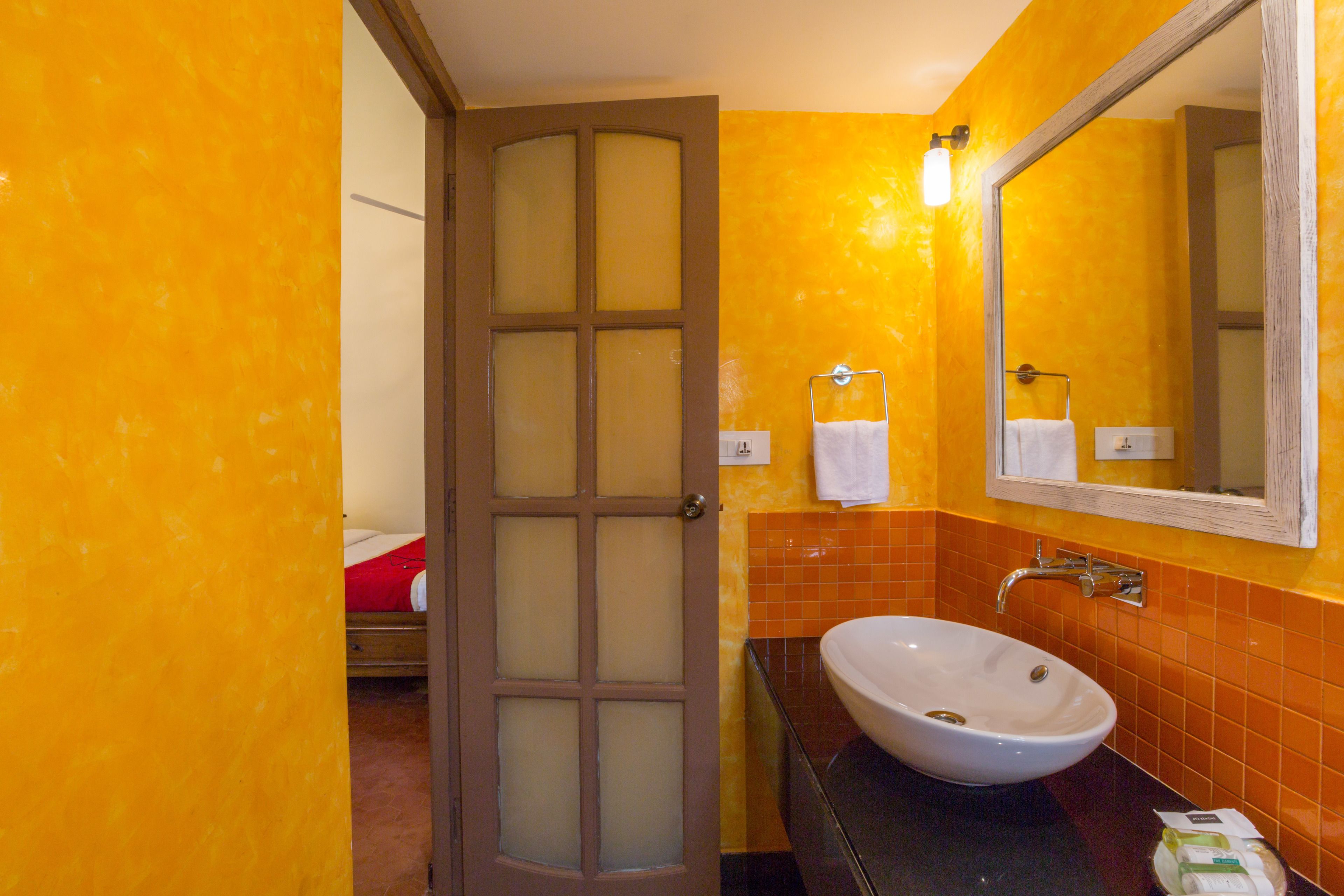 Un baño con un lavabo blanco, paredes con azulejos naranjas, una puerta de madera con paneles de vidrio satinado y un espejo sobre el lavabo.