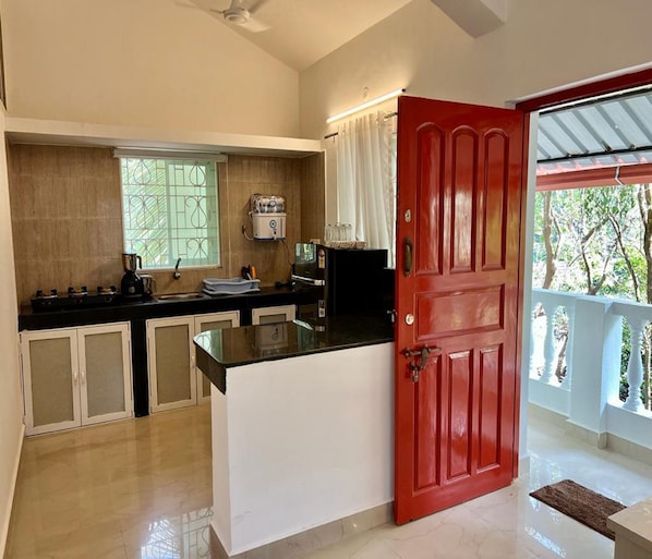 Una cocina con puerta roja, armarios blancos, encimera negra y ventana con celosías decorativas.