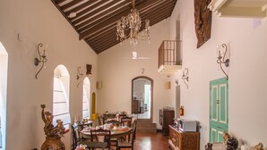 Un comedor con mesas y sillas de madera, un ventilador de techo y una escalera que conduce a un nivel superior.