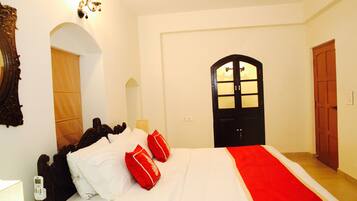 A hotel room with a bed, a bedside table, a lamp, a mirror, and a door.
