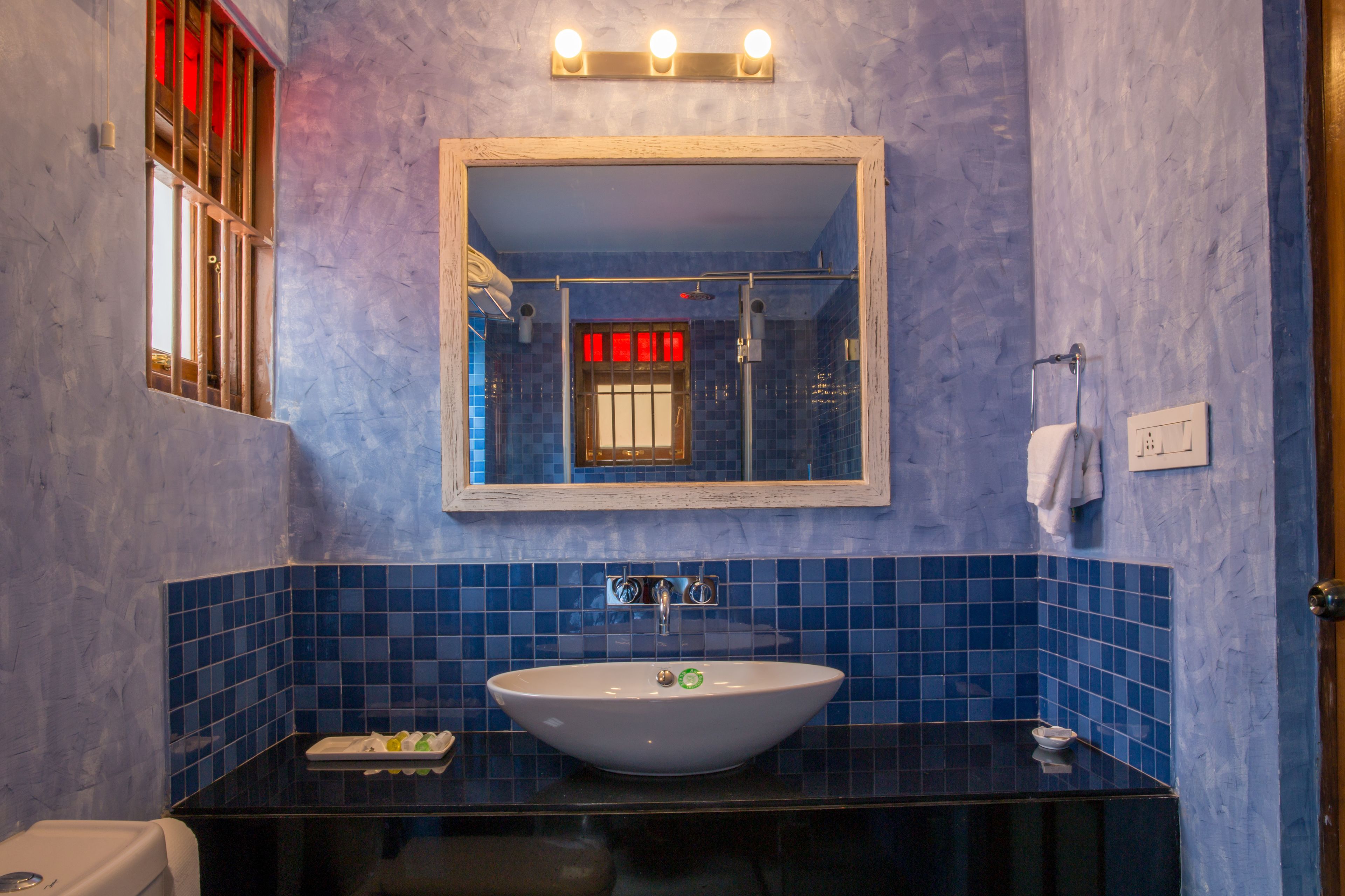 A bathroom with a large mirror, a sink, and blue-tiled walls.