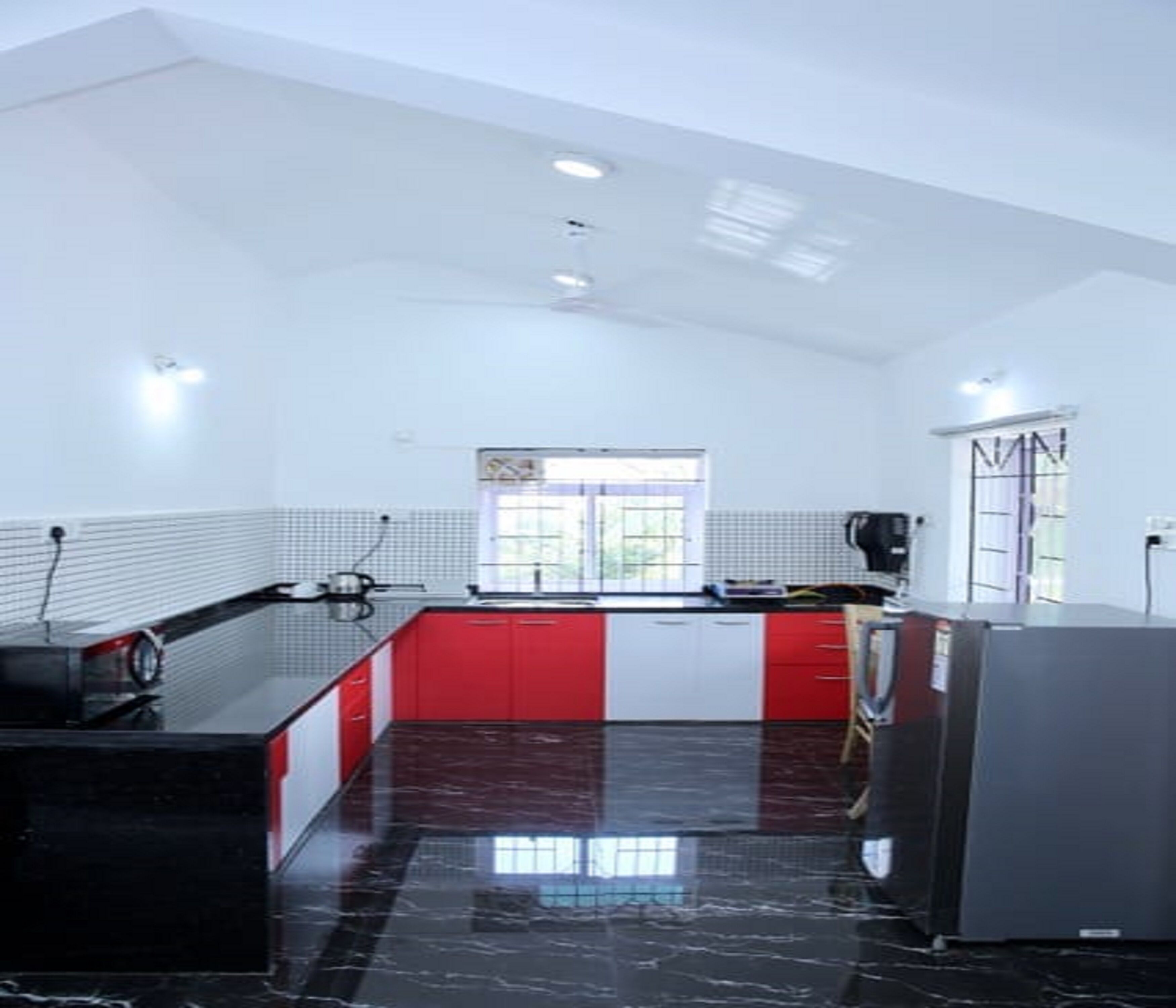 A kitchen with a black marble countertop, red and white cabinets, a window with a view, and a refrigerator.