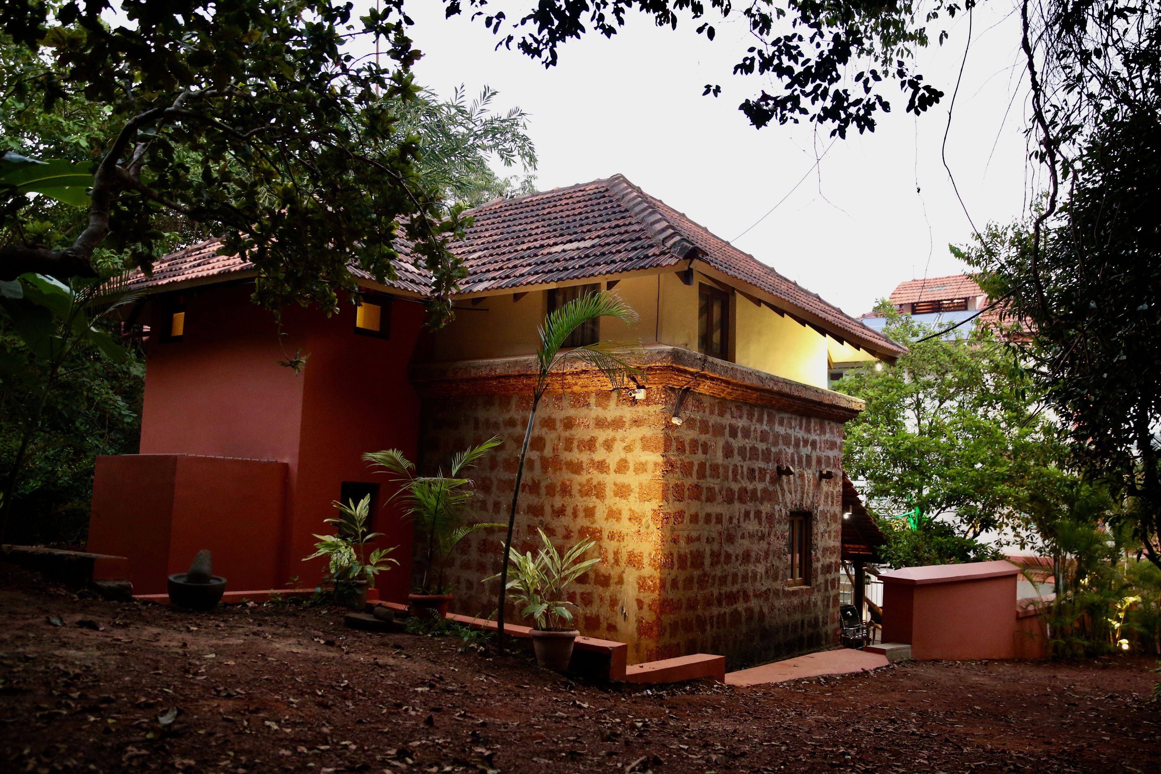 A small, two-story building with a tiled roof and a brick facade, surrounded by greenery.
