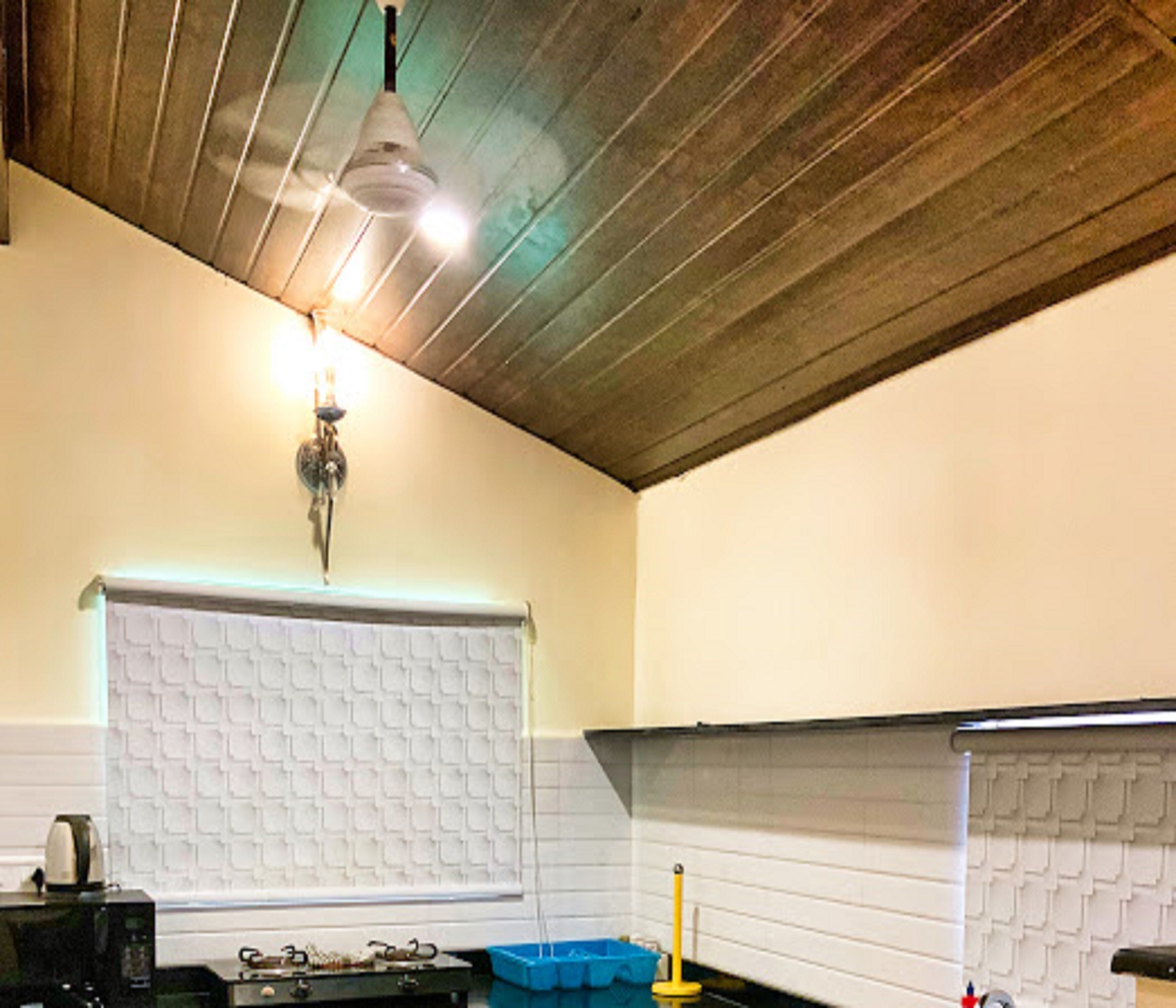 A kitchen with a white tiled backsplash, a hanging light fixture, and a microwave on the counter.