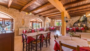 A restaurant with stone walls, wooden beams, and tables set with red tablecloths.