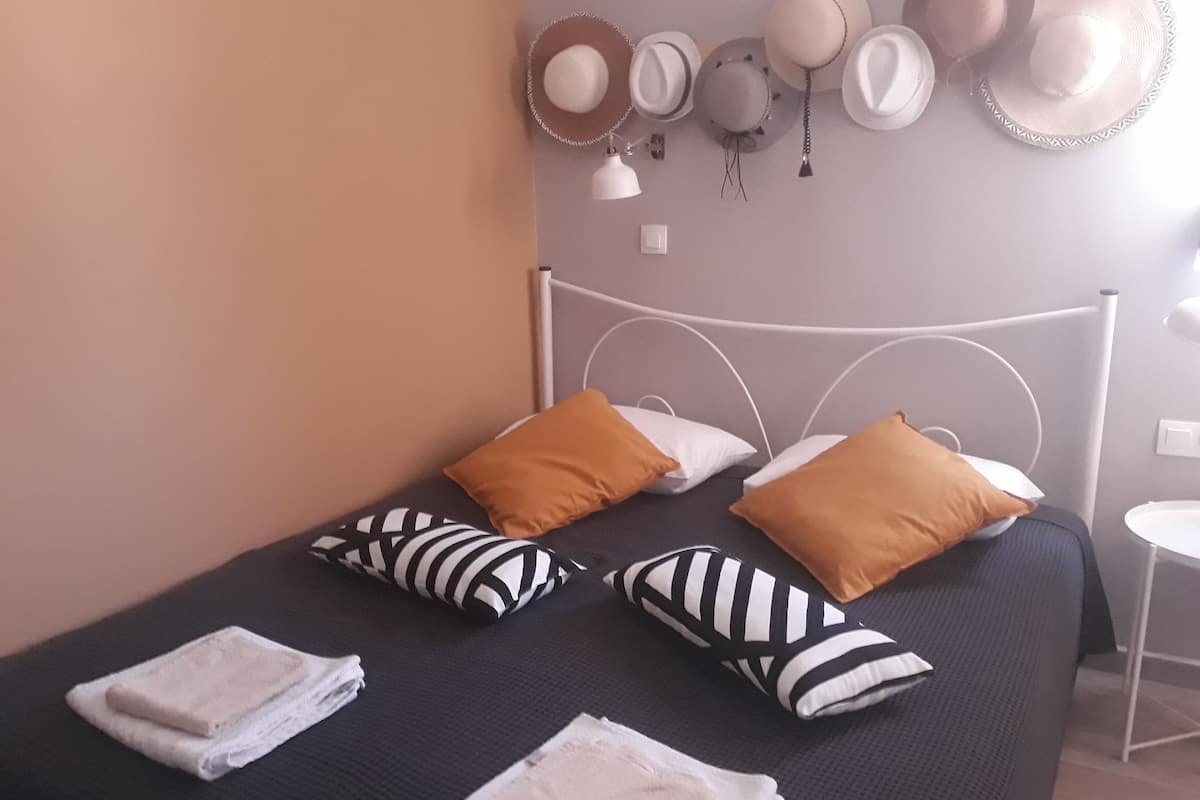 A neatly made bed with striped and solid pillows, a white lamp, and a wall with hats.