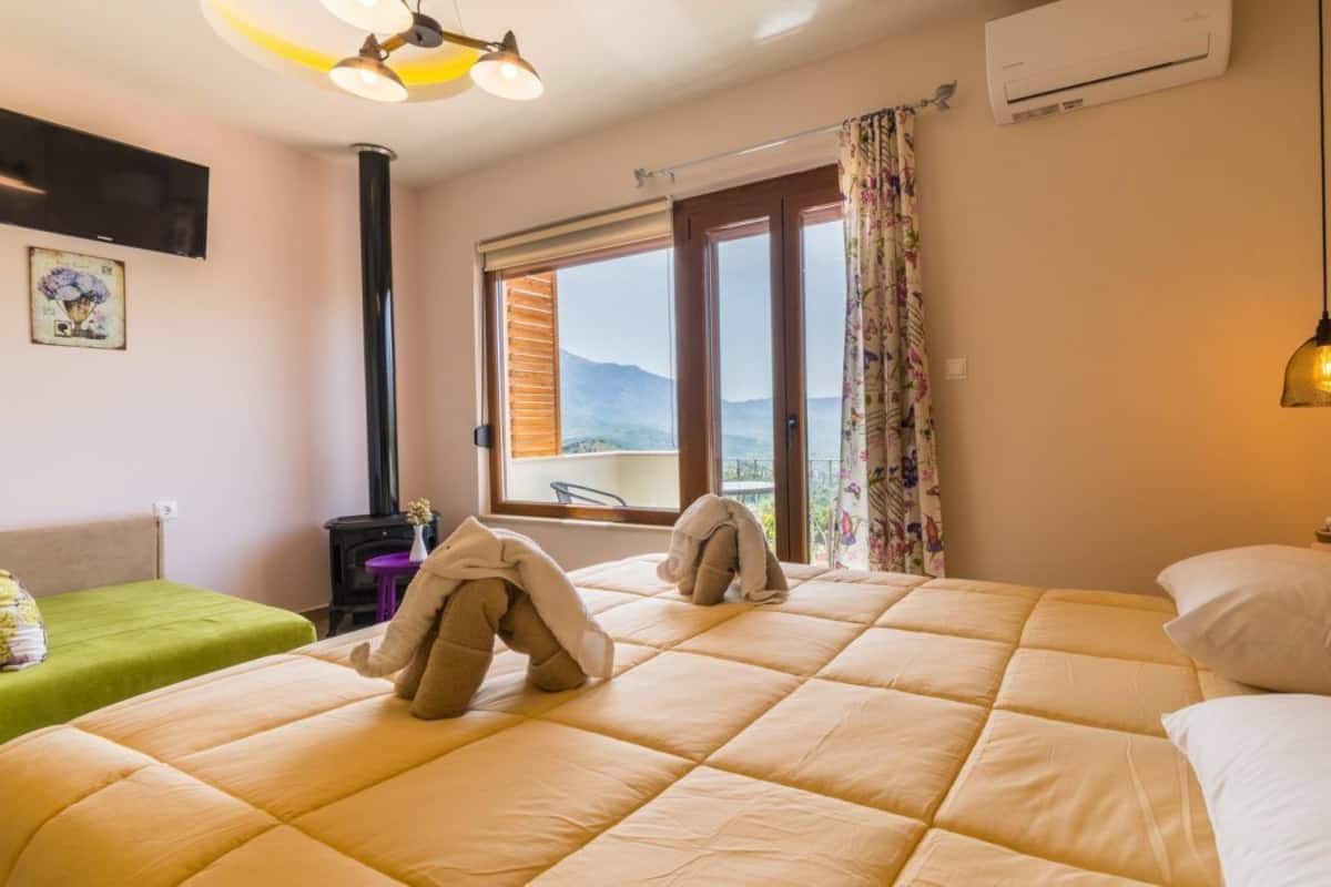 A hotel room with a large bed, a green chair, a window with a view of mountains, and a ceiling fan.
