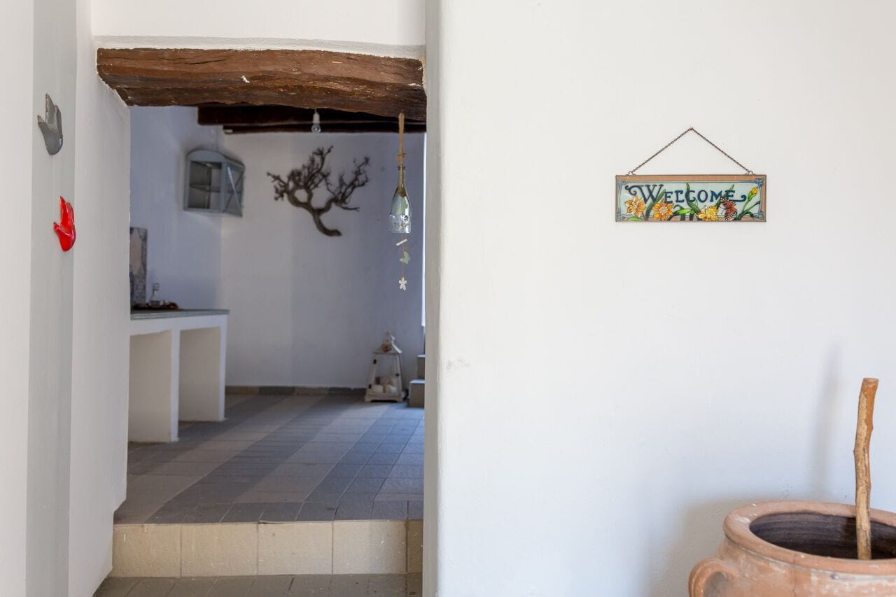 A room with a rustic wooden ceiling, a welcome sign, a potted plant, and a small table with a lamp.
