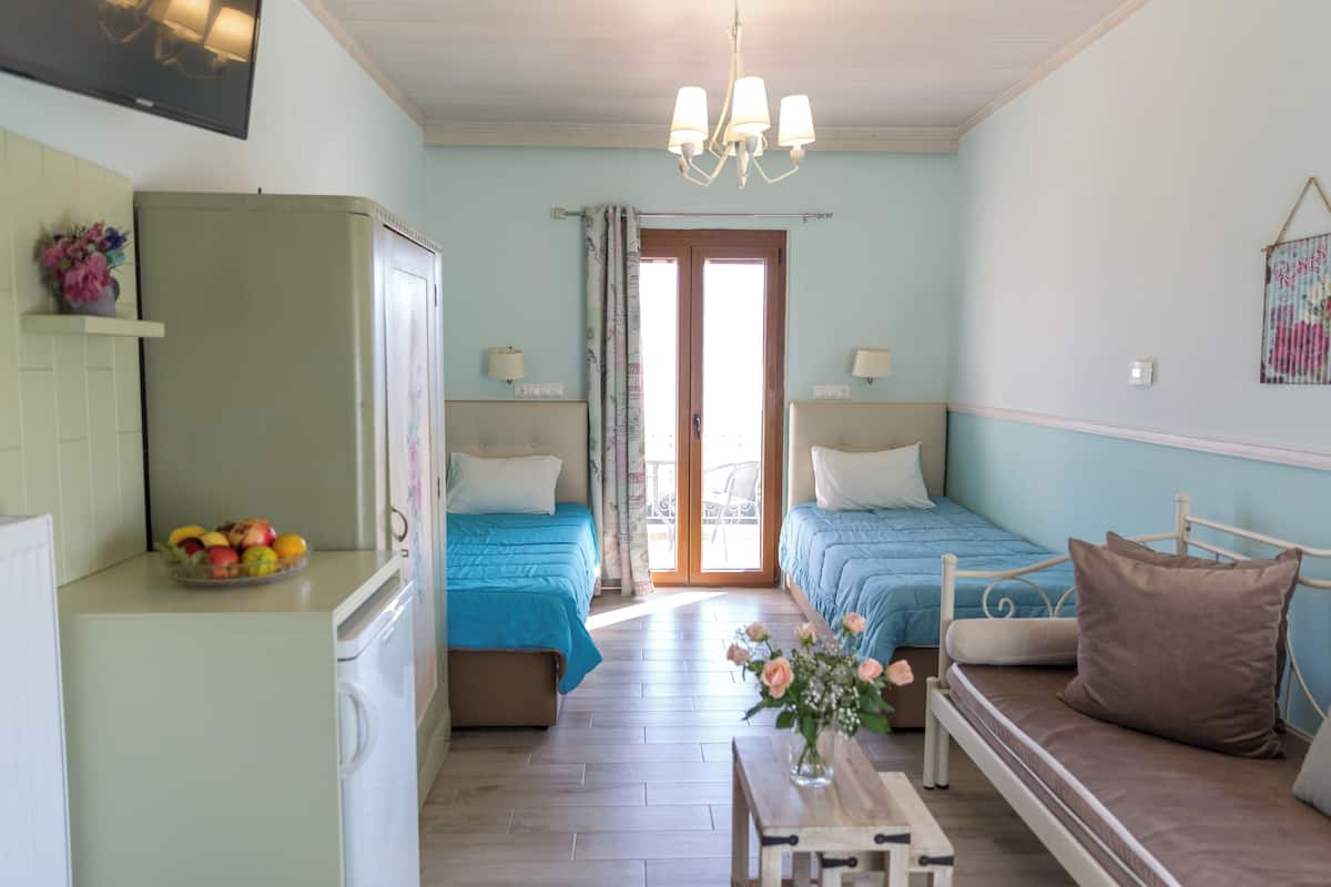 A room with two beds, a dining table, a kitchen area, and a balcony.