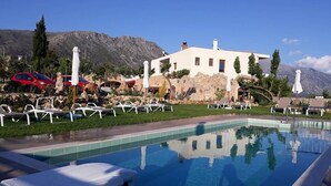 A pool area with lounge chairs, a white building, and mountains in the background.