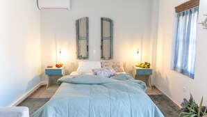 A bedroom with a bed, two bedside tables, a window with curtains, and an air conditioning unit.