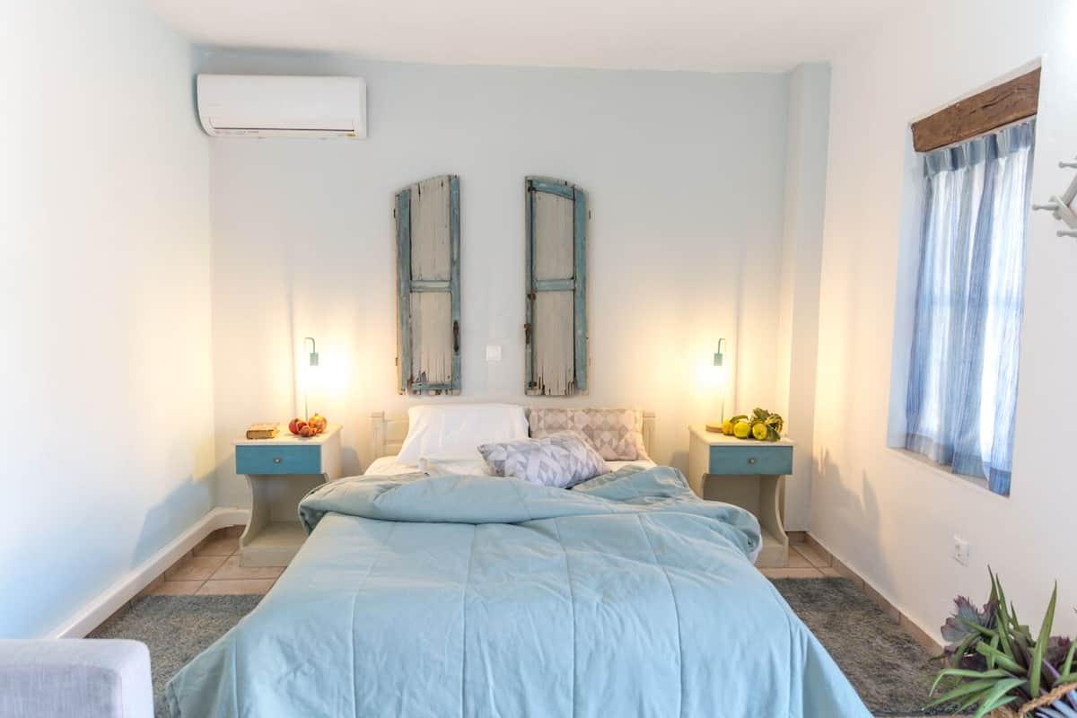 A bedroom with a bed, two bedside tables, a window with curtains, and an air conditioning unit.
