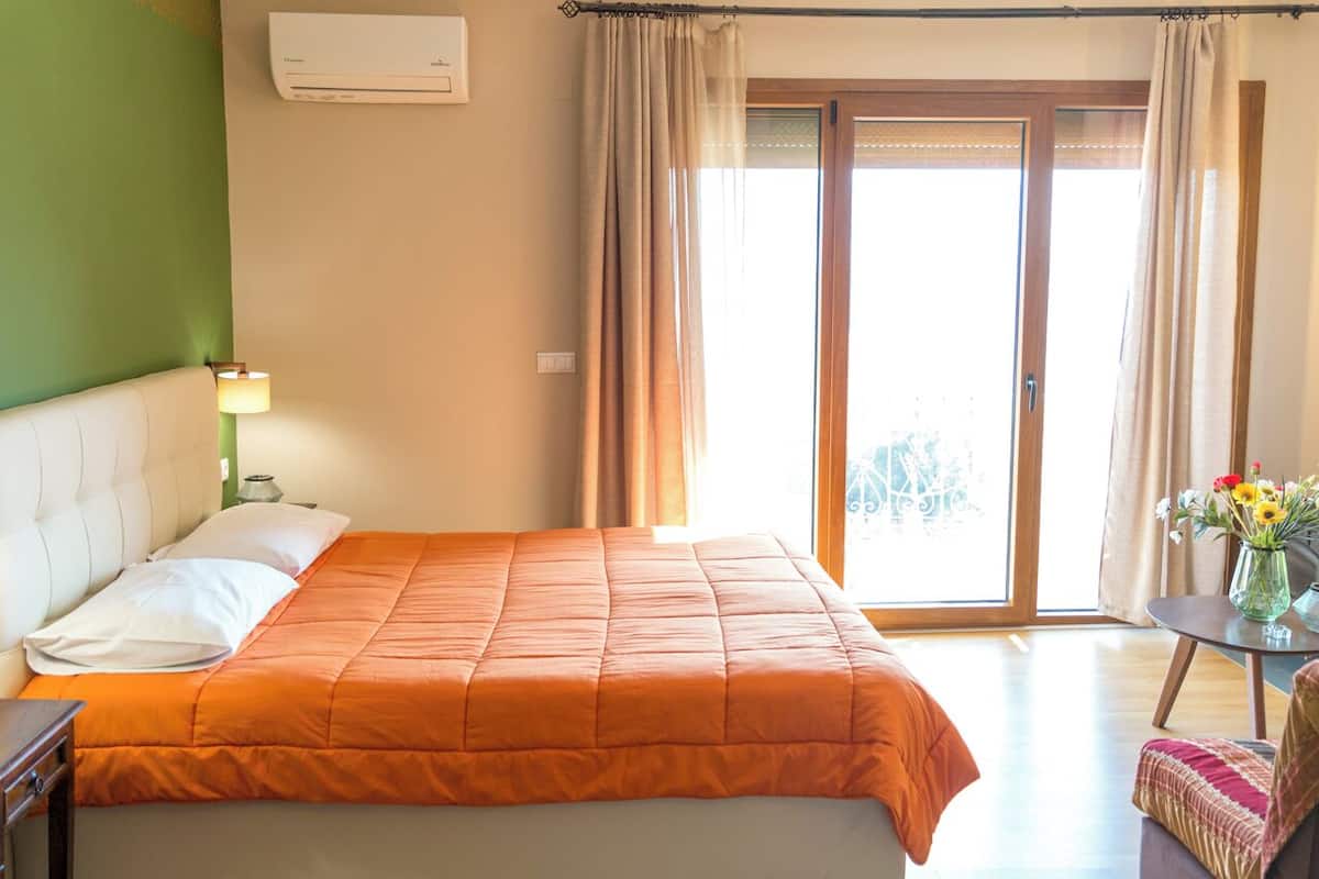 A bedroom with a bed, a nightstand, a lamp, a window with curtains, and a view of the outside.