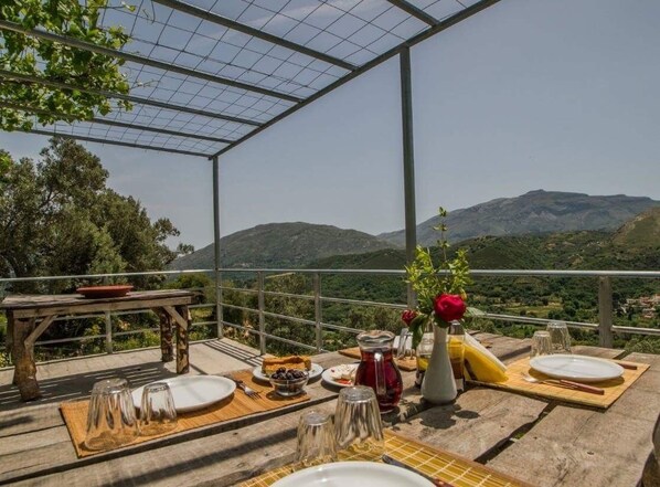 Uma área de refeições ao ar livre com uma mesa posta para dois, com vista para uma paisagem montanhosa.