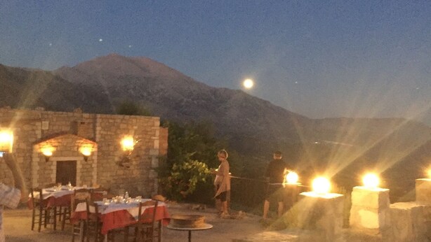 An outdoor dining area with tables set for a meal, a stone building in the background, and a mountain range.