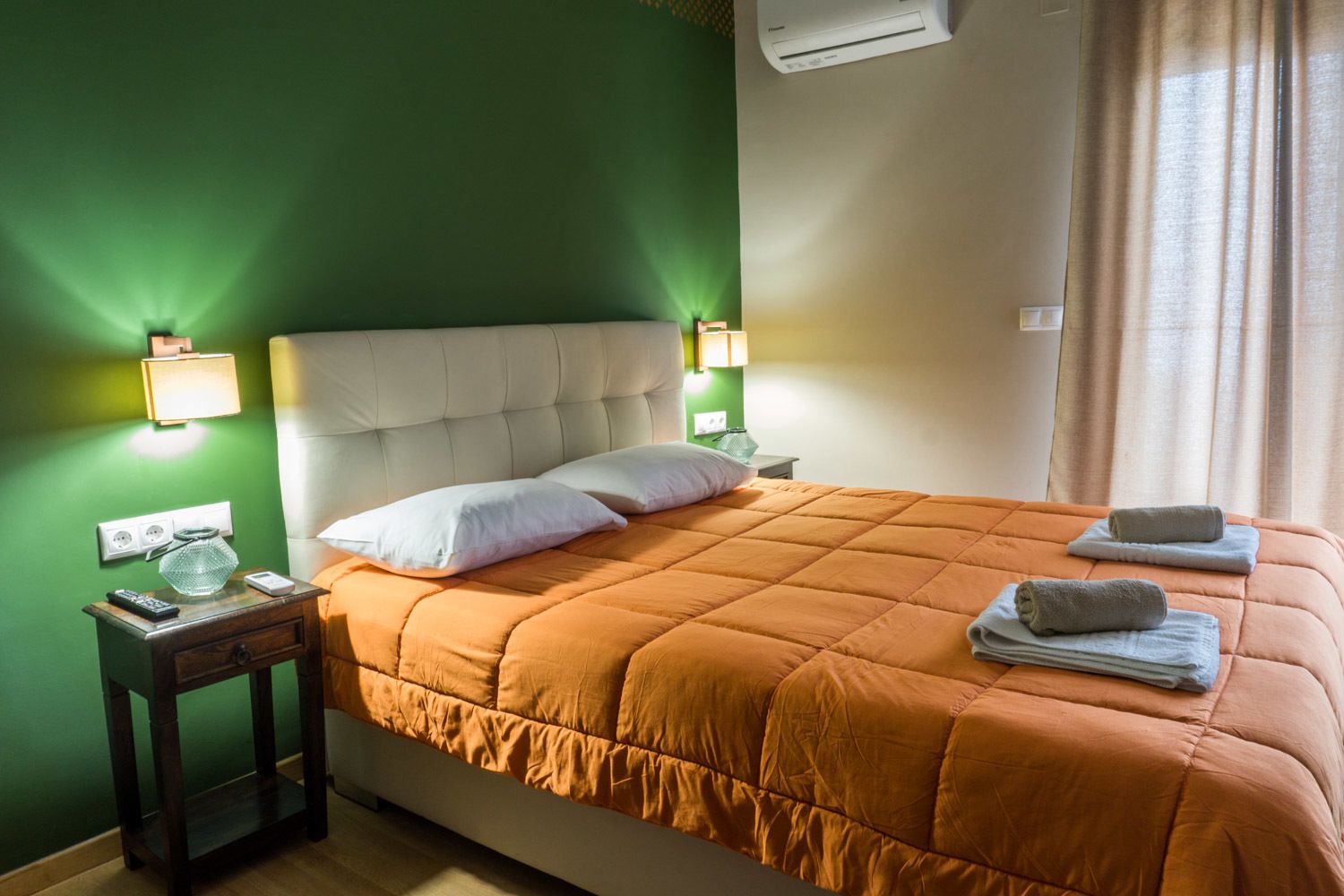 Habitació d'hotel amb un llit gran, dues làmpades de nit, una tauleta de nit amb un comandament a distància i una finestra amb cortines.