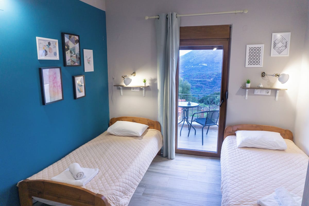 A room with two beds, a balcony with a table and chairs, and artwork on the walls.