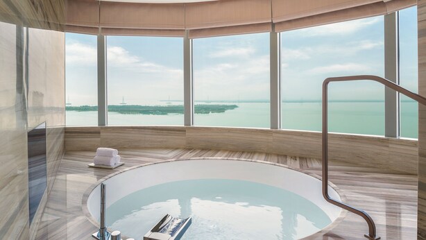 Un baño moderno con una bañera grande, vistas al mar y suelo de madera.