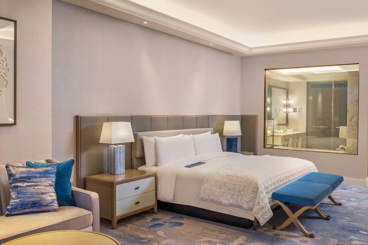 Ett hotellrum med en stor säng, sängbord, en bänk, en soffa och en stor spegel.