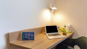 Un bureau en bois avec un ordinateur portable, un téléphone portable, une bouilloire et un panneau.