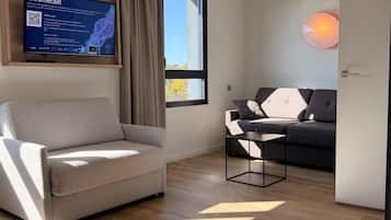A modern living room with a grey armchair, a black and white sofa, a small black table, and a wall-mounted television displaying a Chromecast setup guide.