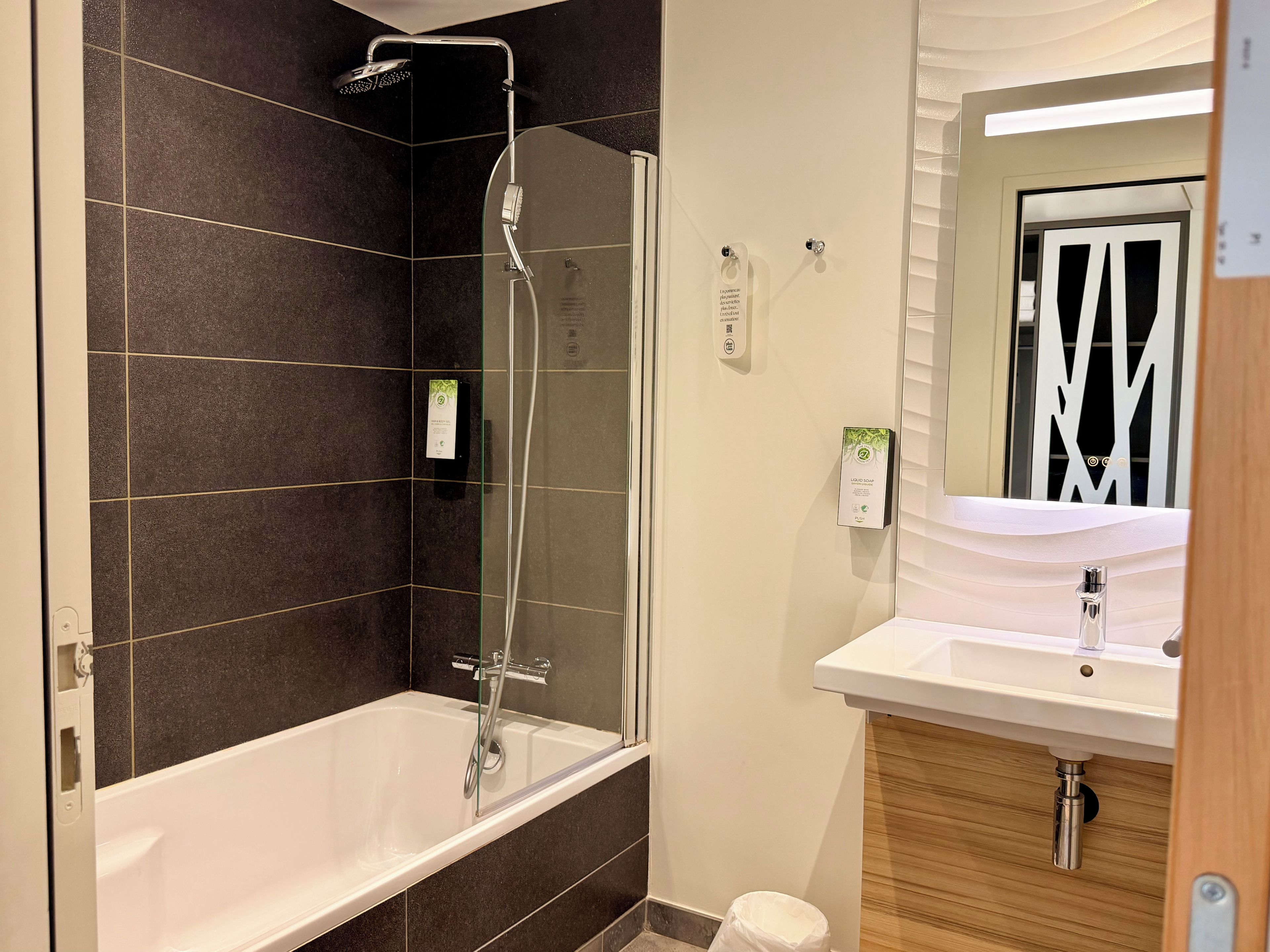 Een moderne badkamer met een douche in een glazen cabine, een witte badkuip en een wastafel met een spiegel.