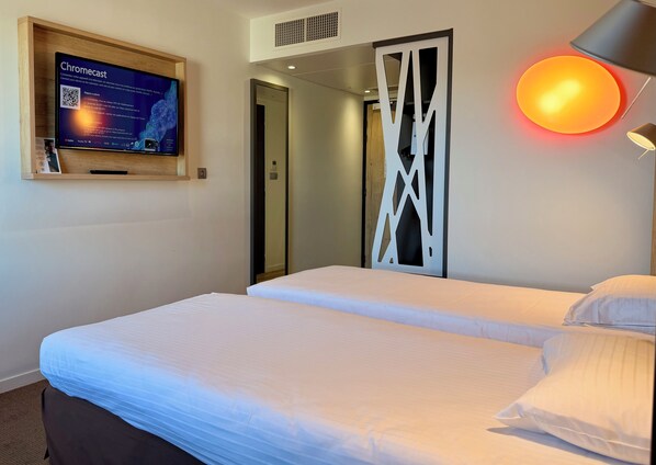 Una habitación de hotel con una cama, un televisor de pared, una lámpara y una puerta.