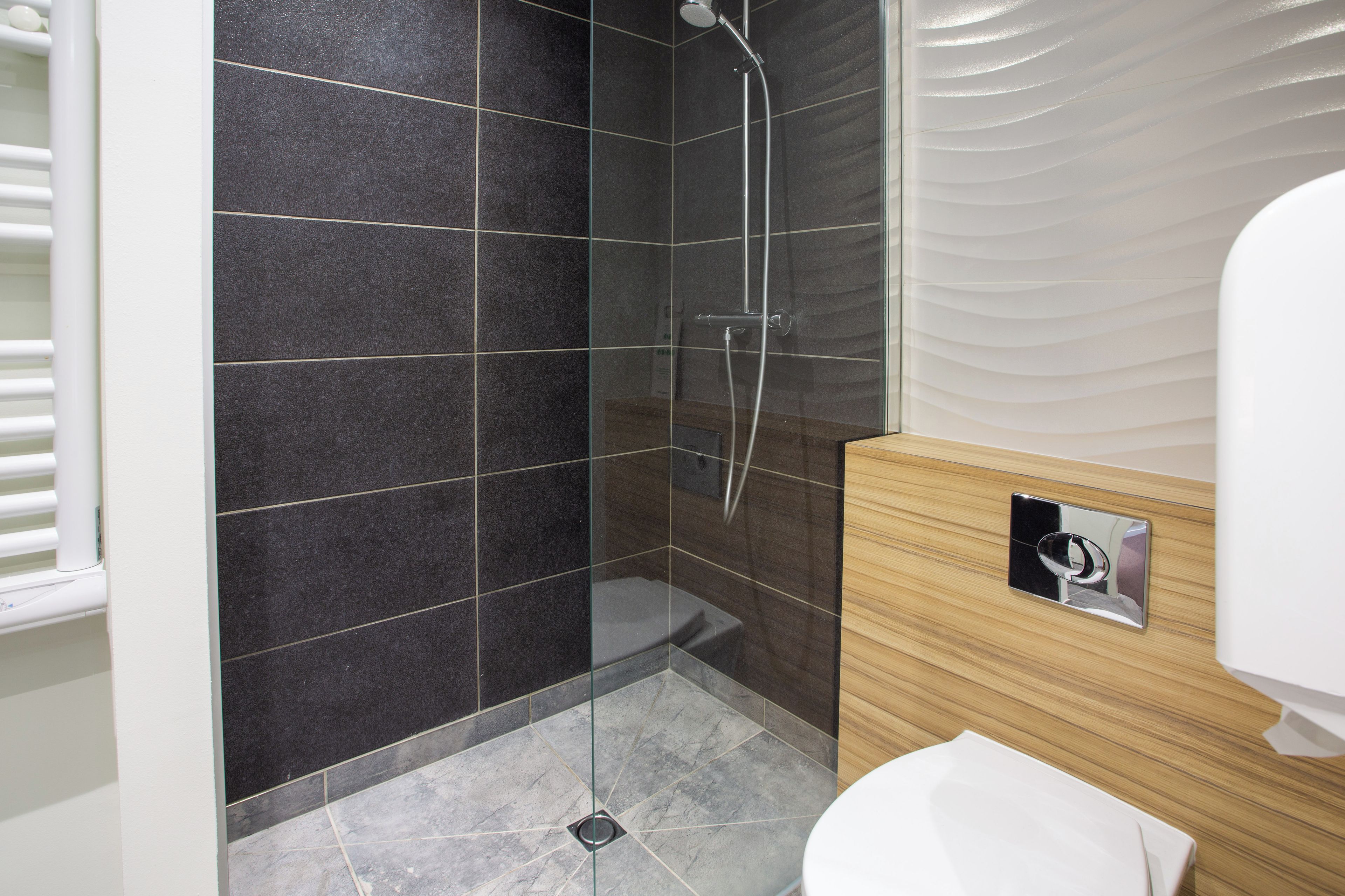 Een moderne badkamer met een douche met glazen wand, een houten wastafelmeubel en een wit toilet.
