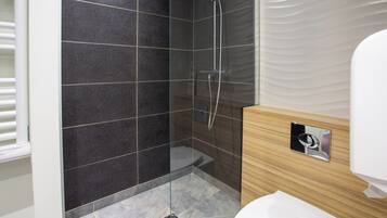 Een moderne badkamer met een douche met glazen wand, een houten wastafelmeubel en een wit toilet.