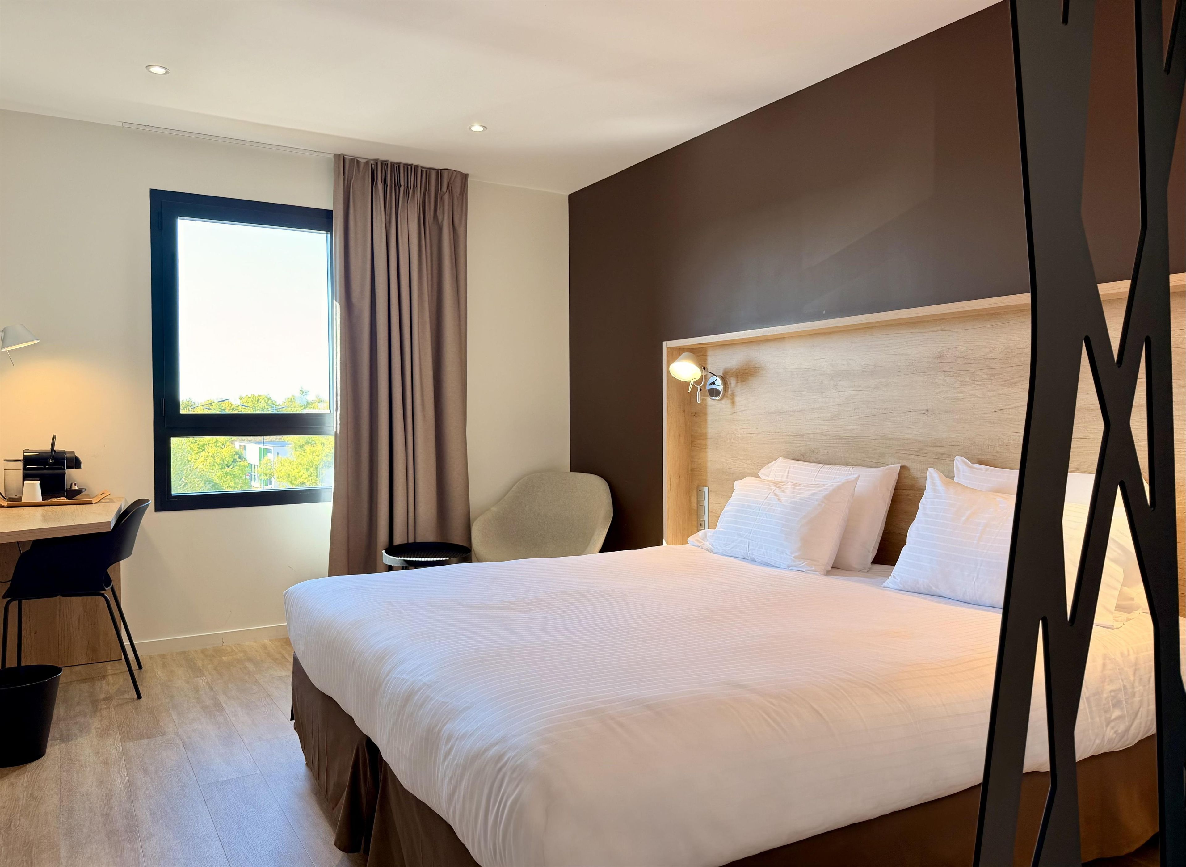 A hotel room with a bed, a desk, a chair, and a window with curtains.