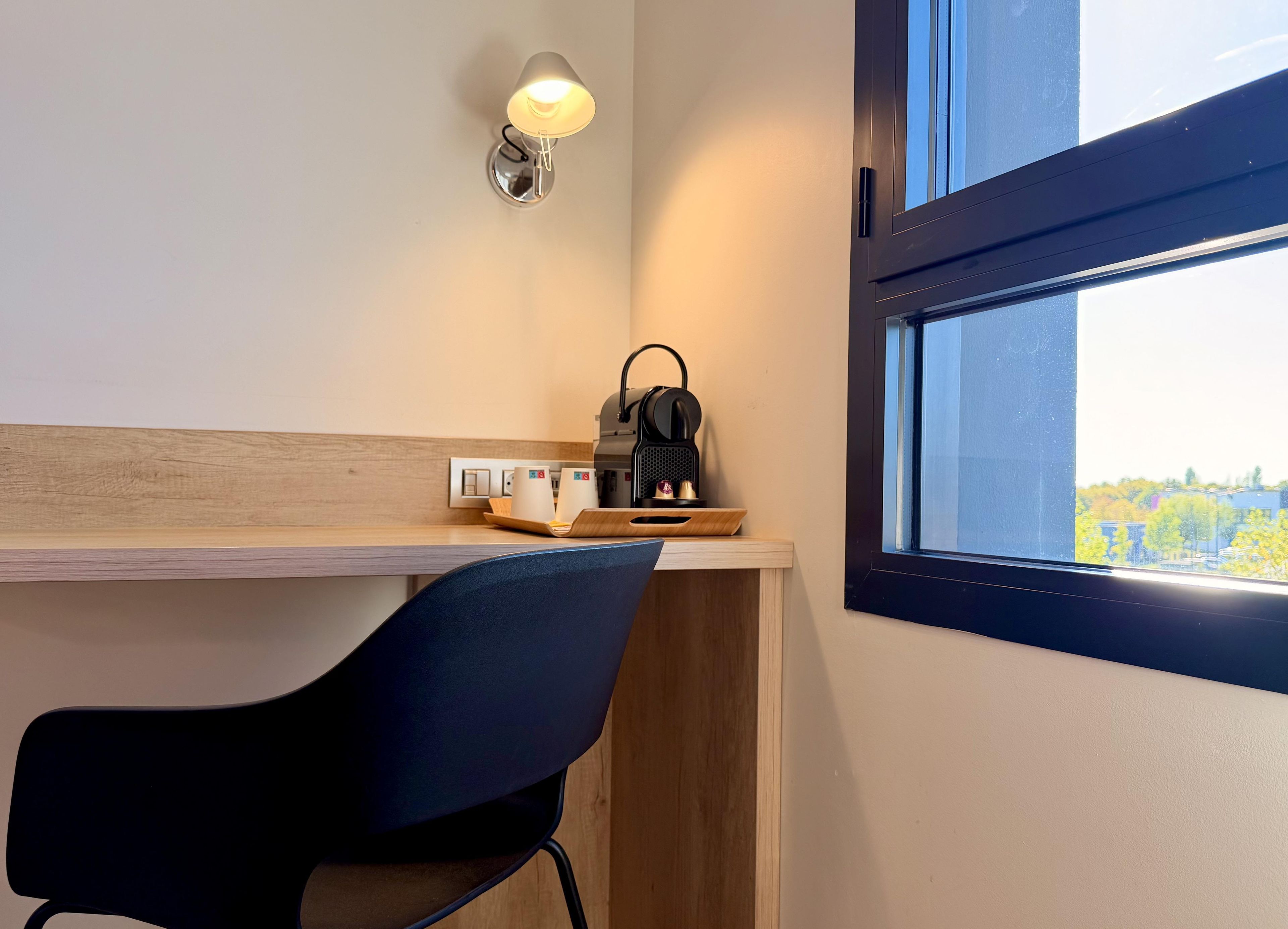 A modern room with a desk, a chair, a coffee machine, and a window with a view.