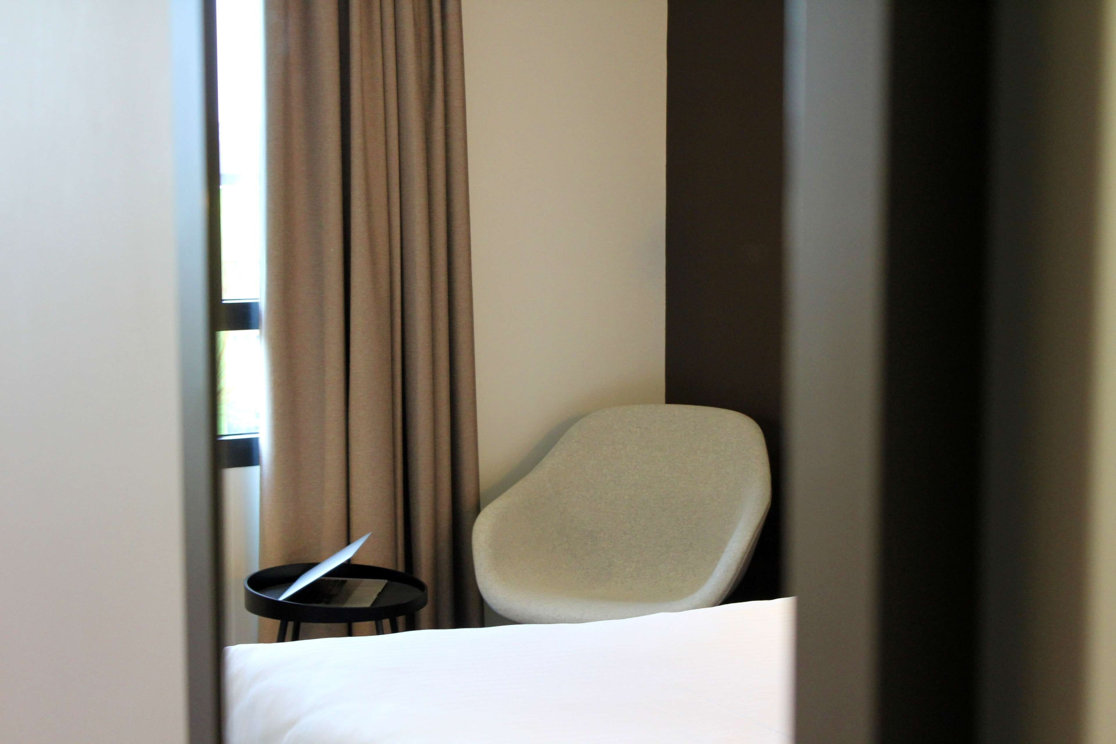 Une chambre d’hôtel avec un lit, une chaise et une petite table sur laquelle se trouve un livre.