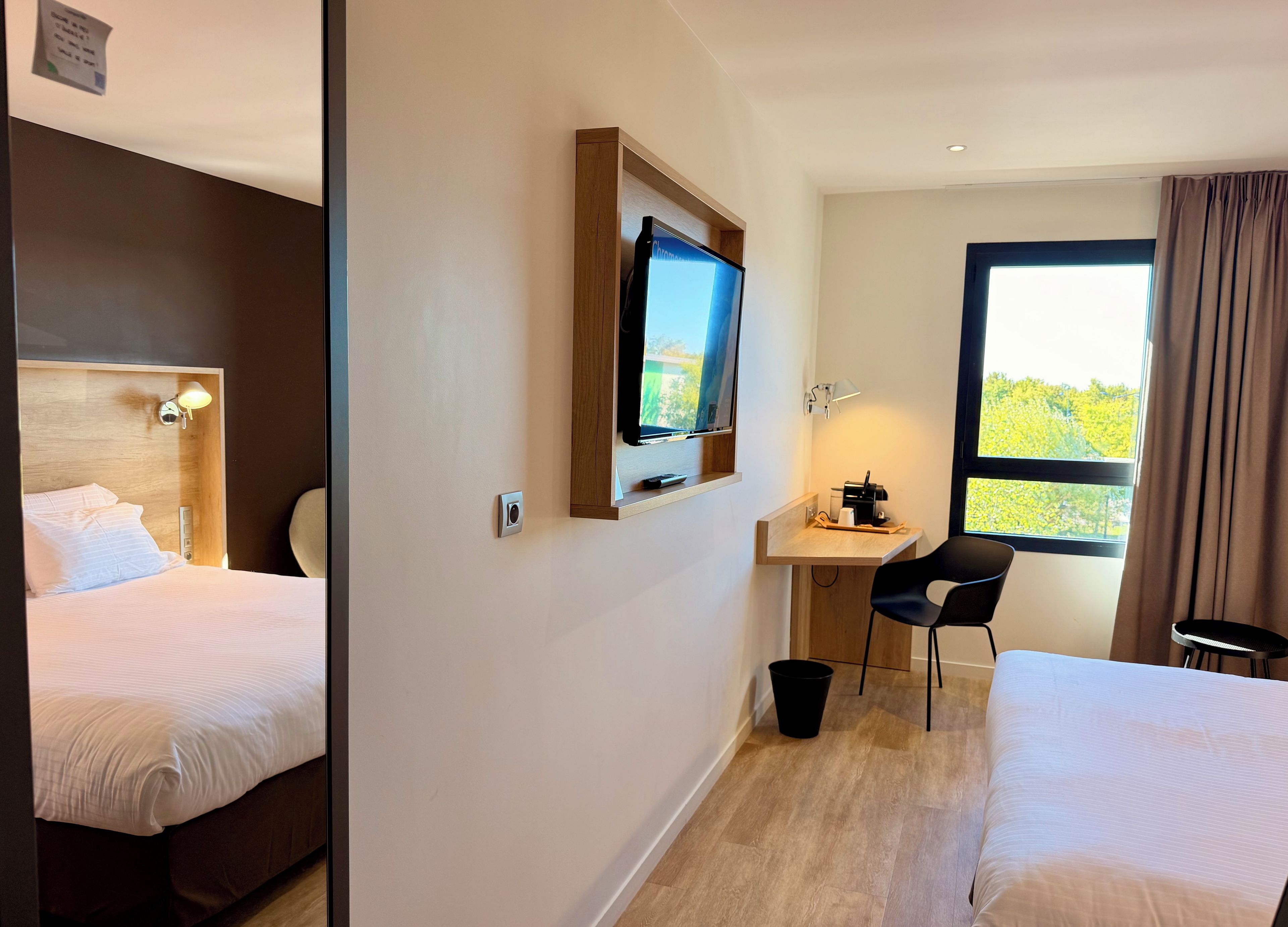 A hotel room with two beds, a desk with a chair, a television, and a window with curtains.