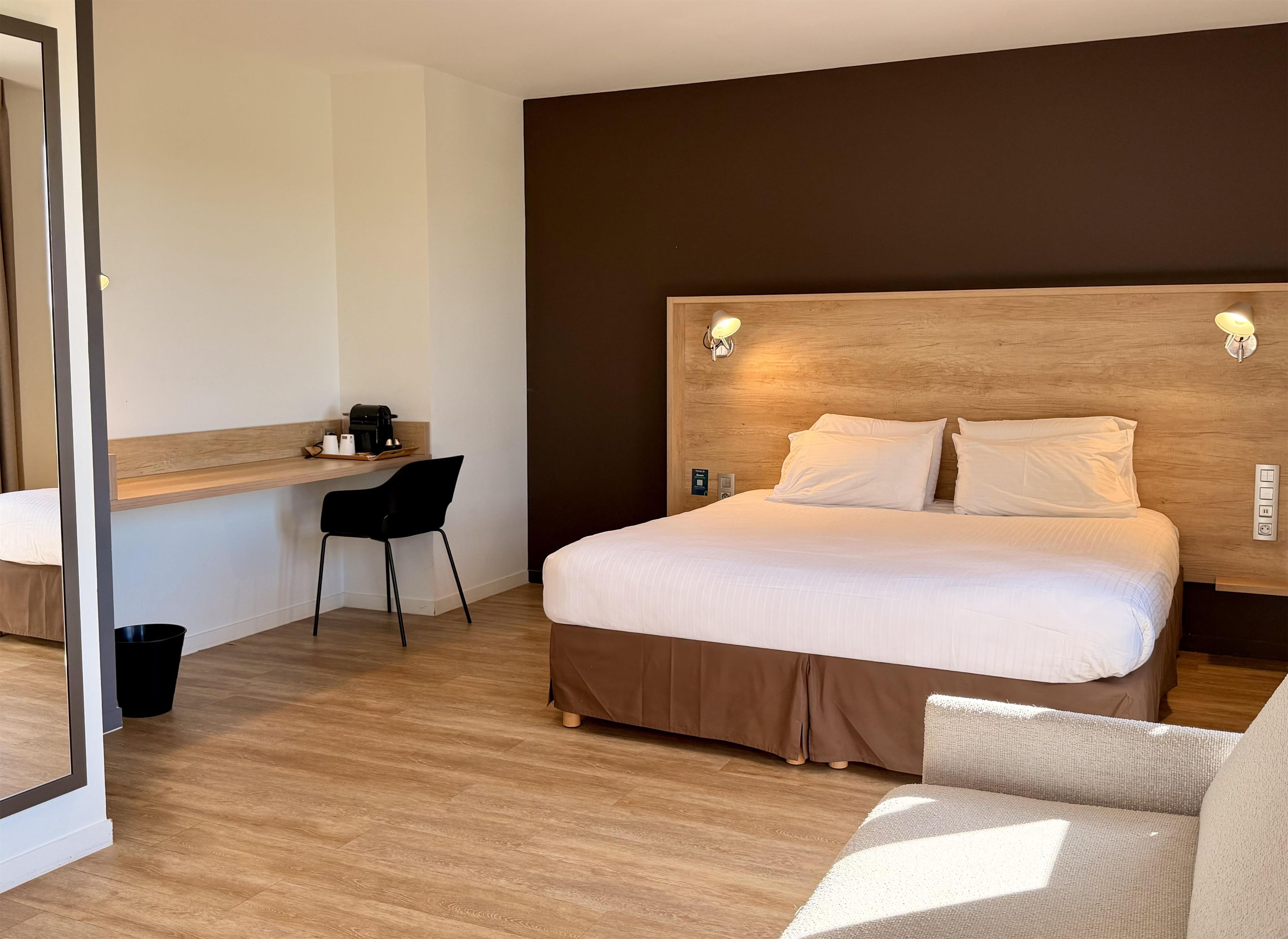 Una habitación de hotel con cama, escritorio, silla y un cubo de basura pequeño.
