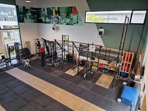 Un gimnasio con diversos equipos de ejercicio, un televisor montado en la pared y un cartel que dice 'risque collectiveités'.