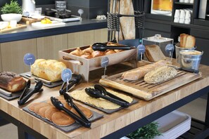 A buffet counter with various breads, pastries, and a coffee machine. - Campanile PRIME - Laval Nord (Change)