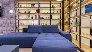 Een moderne woonkamer met een hoekbank, inbouwplanken met planten en een flatscreen televisie aan een gestructureerde muur.
