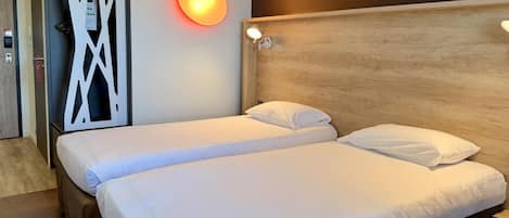 A hotel room with two beds, a wooden headboard, a wall-mounted light, and a decorative panel.