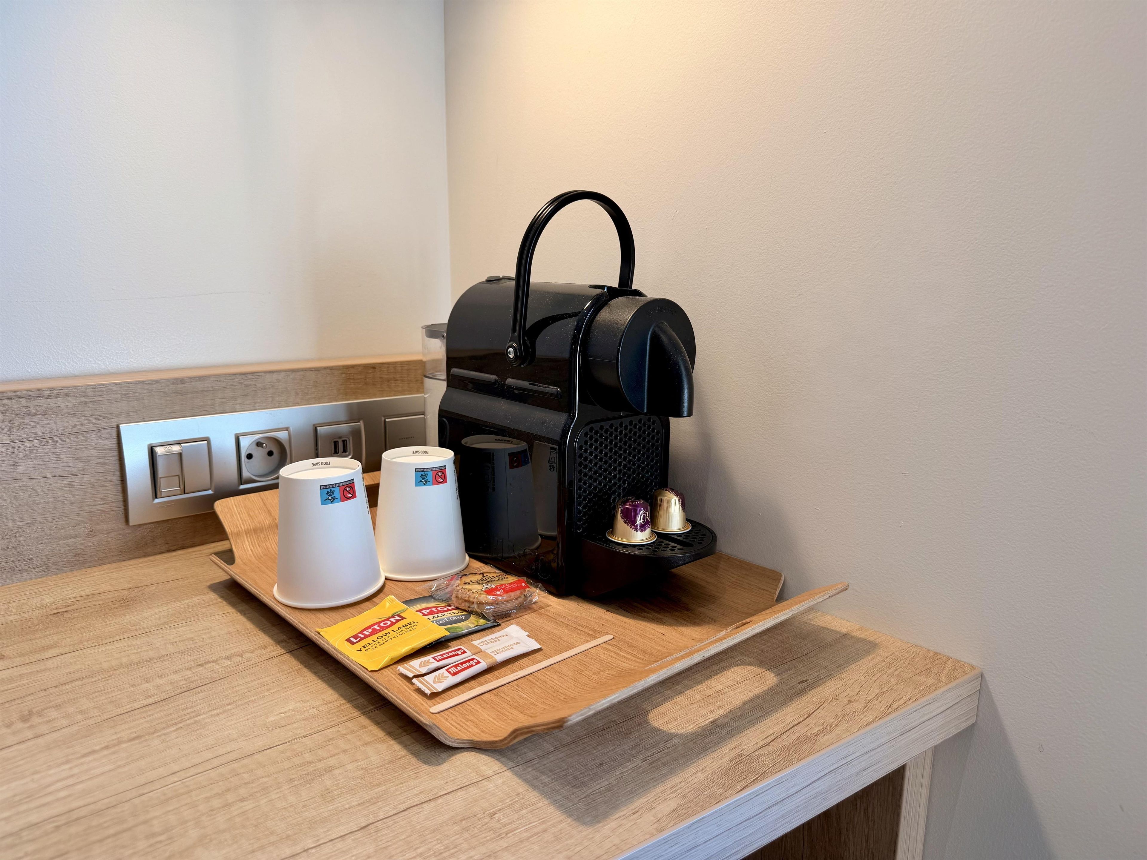 A coffee machine with disposable cups and a tray with snacks and a drink.