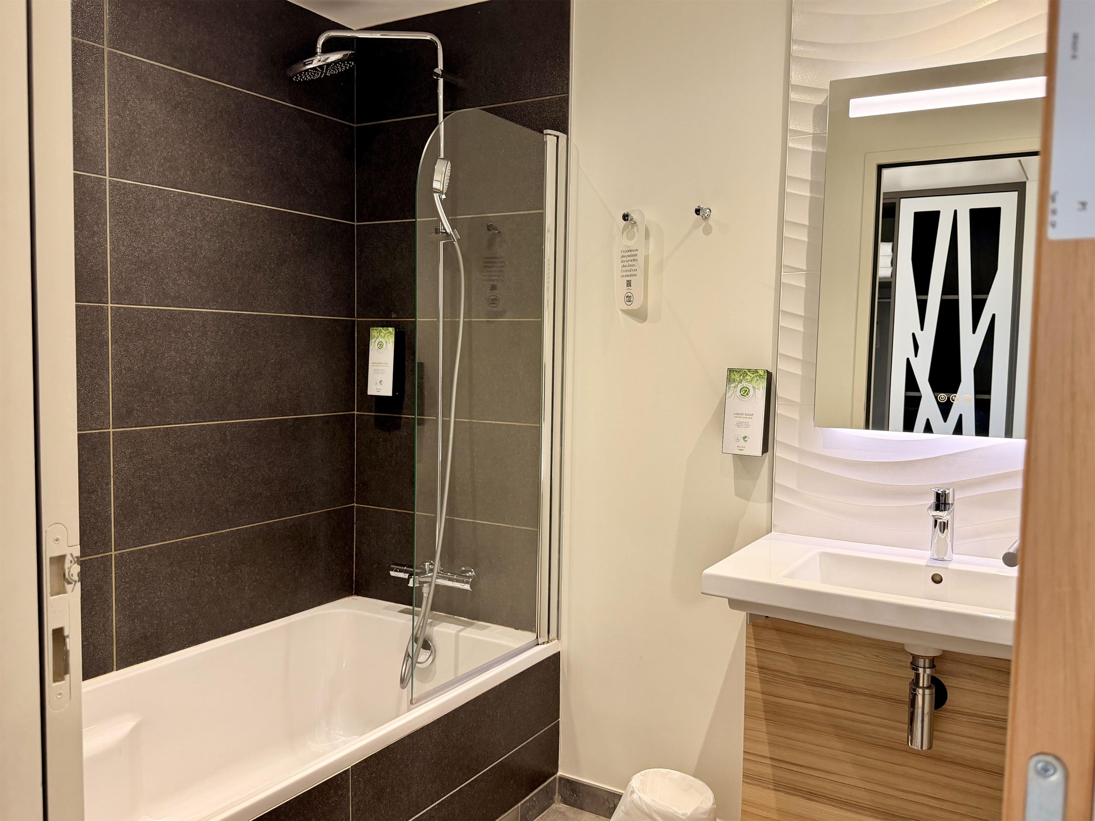 Un baño moderno con ducha envuelta en cristal, una bañera blanca y un lavabo con espejo.