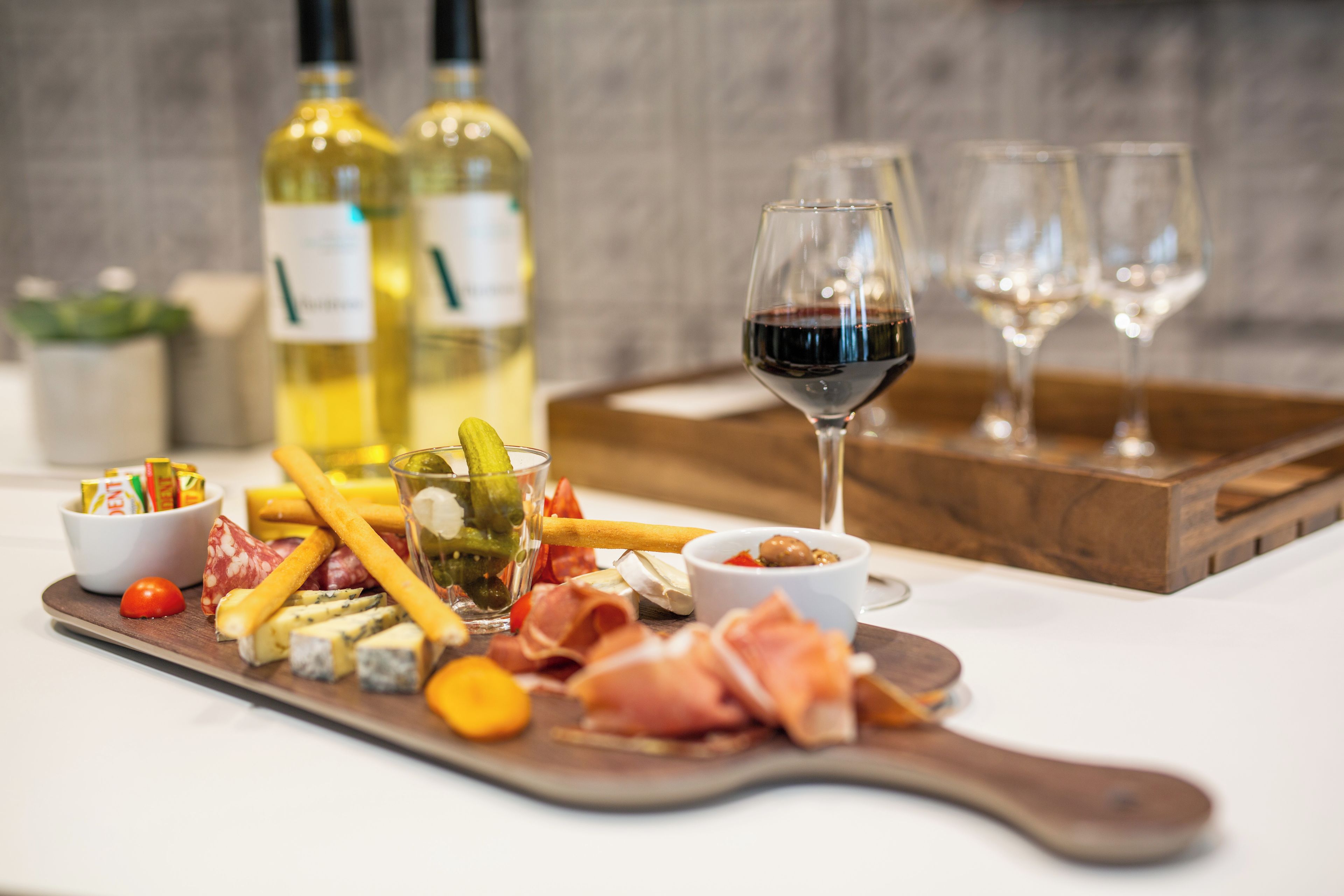A charcuterie board with various cheeses, meats, and pickles, accompanied by wine glasses and bottles.