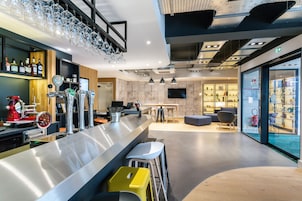 Un área de bar moderna con una barra de acero inoxidable, varias griferías de cerveza y una disposición de asientos con taburetes.