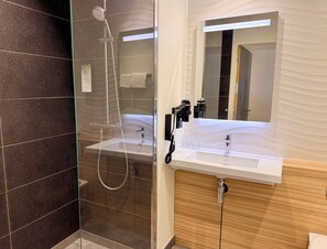 Un baño moderno con ducha de vidrio, tocador con espejo y lavabo.