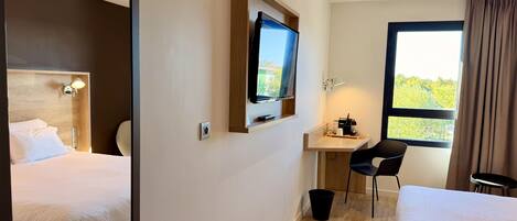 Habitación de hotel con dos camas, un escritorio con silla, televisión y ventana con cortinas.
