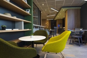 A modern cafe with round tables, green and yellow chairs, wooden shelves, and a geometric wall design. - Campanile PRIME - Montpellier Centre St Roch (Montpellier)