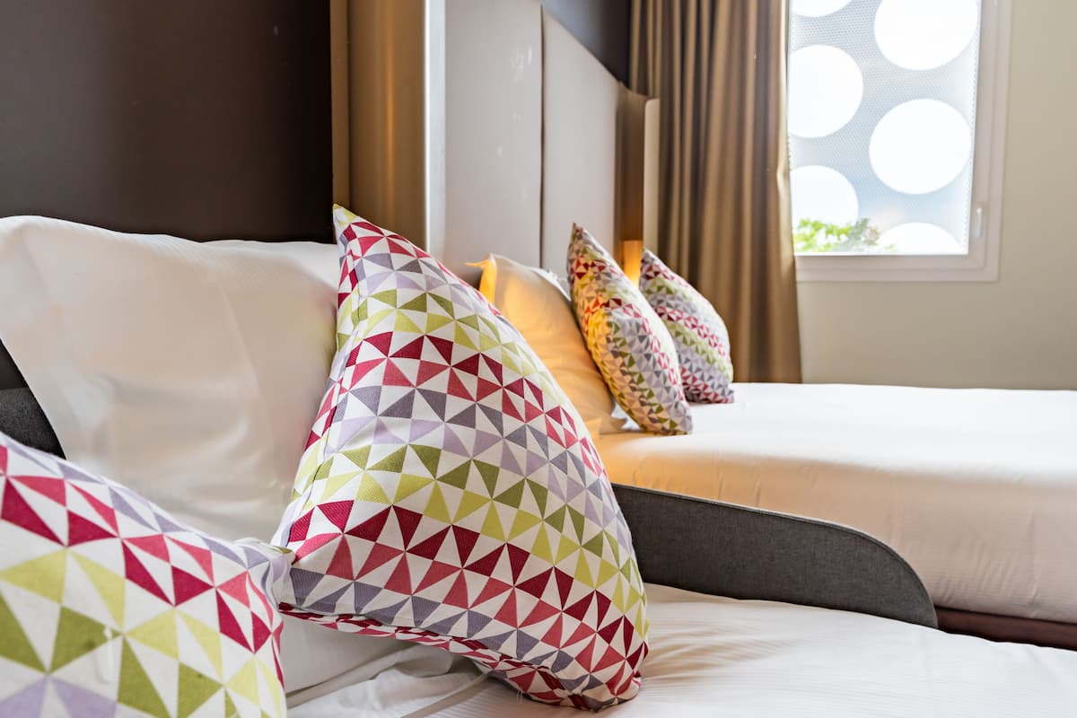Une chambre d’hôtel avec un lit, plusieurs oreillers, une fenêtre donnant sur un paysage agréable et une tête de lit.